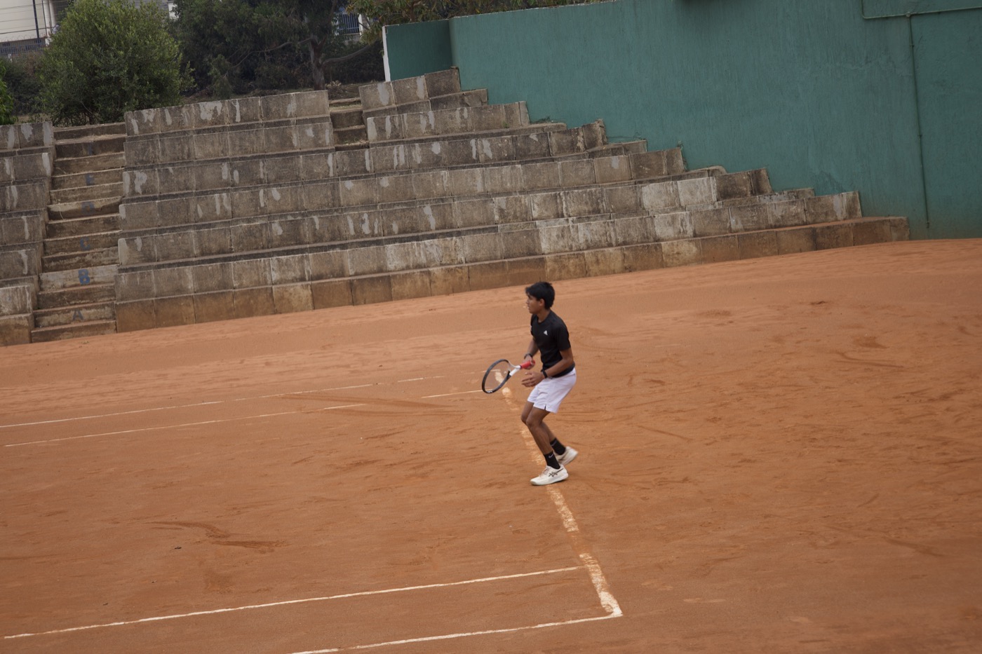 Player in ready stance with tiered stone bleachers behind the court