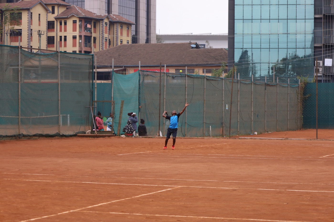 Player mid-serve with the Nairobi skyline towering behind the court