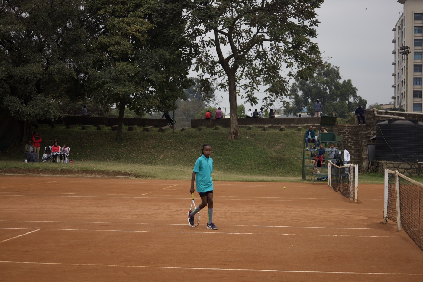 Player on the baseline with spectators watching from the grassy hillside