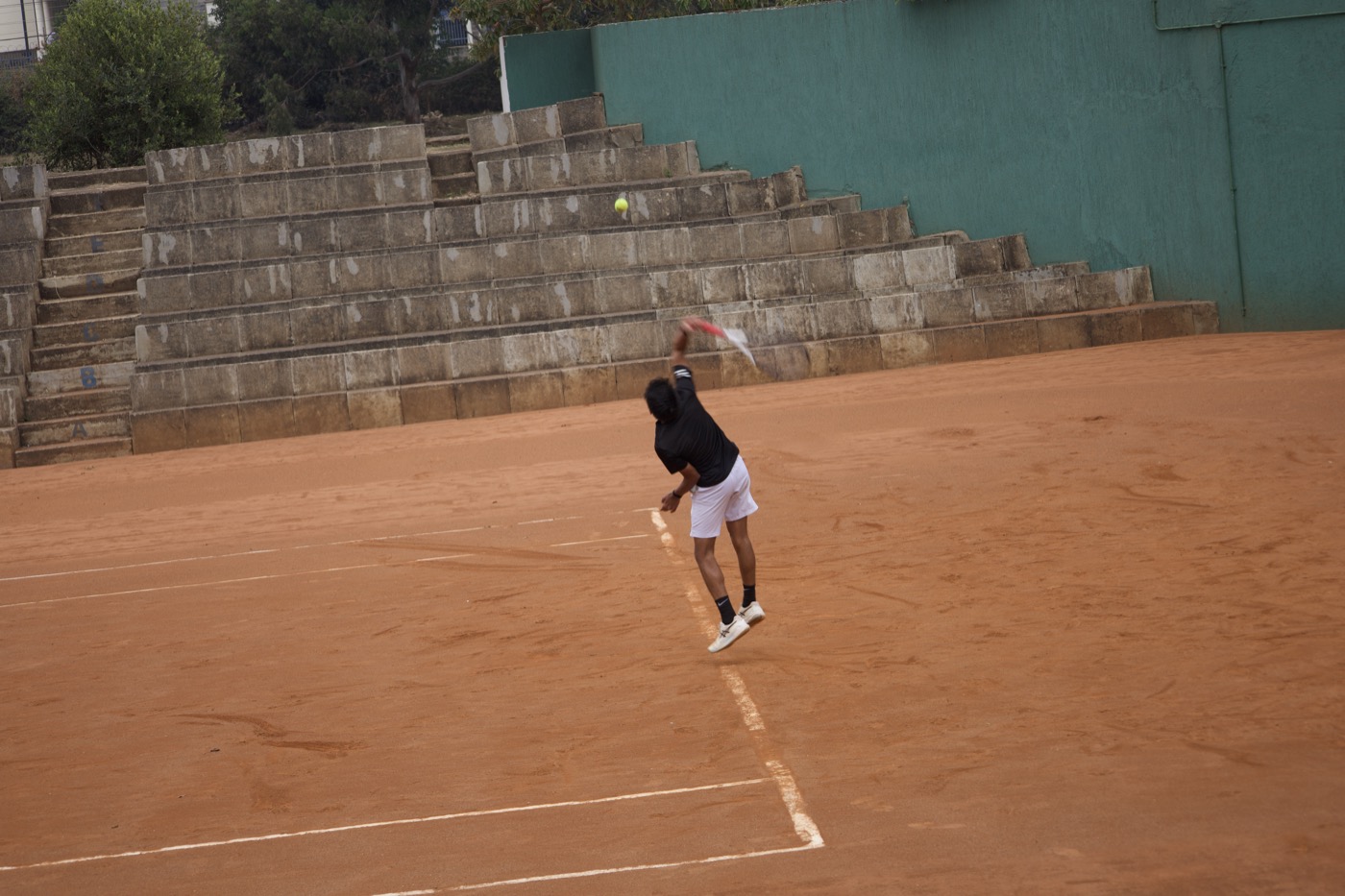 Player mid-serve with tiered stone bleachers behind the court